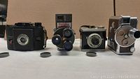 Four cameras shown from front, two movie and two film cameras with lens caps in front.