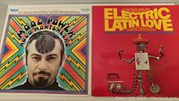 Front covers of two vinyl albums: Moog Power album with psychedelic colorful cover featuring face with electronic brain, and Electric Latin Love with metal robot in sombrero