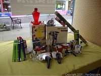 Photo showing various kitchen gadgets arranged on a table including an electric juicer, boxed Trudeau cheese grater and garlic press, pepper mill, pickle forks, and other utensils.