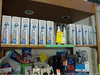 Shelf with 11 boxed Stubby Cooler Flask water bottles, all new and unopened, stacked side by side. Shows packaging and product design.