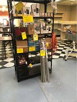 Full shelving unit view showing boxes of common nails, red bin of hardware packages, carpet trim strips and extension cord