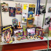 Overview of children's craft and play items displayed on shelf, showing various boxed craft kits, games, toy mops, and accessories.