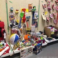 Wide view of assorted toys including outdoor toys, games, and craft kits on shelf against pegboard wall.