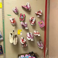 Assorted men's and women's footwear hanging on pegboard including boat shoes, sandals, and multiple pairs of flip-flops in white, pink, and orange with various strap colors.