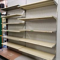 Front view of two metal shelving units mounted side by side with multiple shelves and pegboard backing; shelves are worn and cream colored.