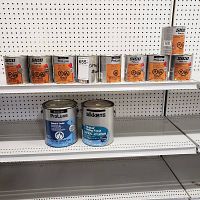 Nine quarts and two large cans of wood finish and stain on metal shelving with pegboard background.