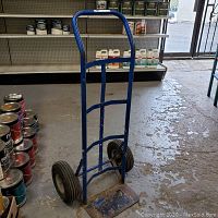 Full view of the blue metal hand cart standing upright showing frame, handle and wheels.