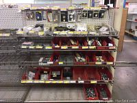 Overview of four metal shelves with red bins holding assorted electrical parts