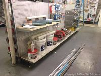 Shelves with wallpaper rolls, buckets of adhesives, and extension cords on bottom shelf.