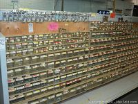 Front view of plywood board with multiple rows of clear plastic bins filled with assorted screws, nuts, bolts and anchors beneath a pegboard top section displaying packaged hooks