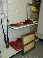 Wide view showing large blue bolt cutters, red trays with assorted tools on a shelf, and stacked tin ceiling panels leaning against shelf.