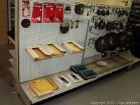 Pegboard display shelf showing packs of 3M sandpaper sheets, hook and loop tack pads and rectangular sanding sponges