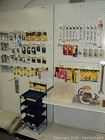 Display of various tools and hardware including wrenches, circular saw, trowels, and door hardware arranged on pegs and table.