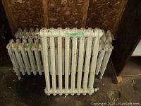 Two white-painted cast iron radiators leaning against a plywood wall with a third partially visible behind.