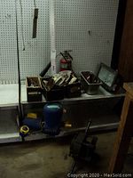 Photo showing wooden boxes on a shelf containing various hand tools, carpenter's square, metal ruler, fire extinguisher, copper strapping rolls, and saw blades. Blue Goulds circulation pump visible below shelf.