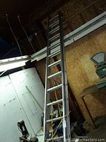 Full view of the 24 ft aluminum extension ladder leaning against a wall inside a workshop or storage area.