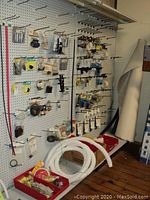Overall display of pegboard with packaged marine supplies, red bins with hardware, coiled hoses and partial roll of flooring leaning against wall.