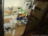 Photo of shelving with various navigation and marine items: wooden ships in bottles, battery chargers in boxes, barometer, compass, cables and belts.