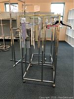 Photo of two chrome finish metal display racks with hanging rods and wheels positioned on carpeted floor in retail environment