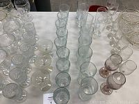 Full view of multiple rows of clear drinking glasses, some patterned, others plain, on a table