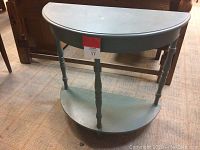 Front view of wooden half-moon shaped vintage hallway table with bottom shelf and turned legs showing wear and distressed shabby chic paint.