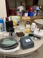 Photo showing a variety of small kitchen appliances arranged on a round table including coffee makers, a food processor, electric skillet, and other gadgets in different colors and sizes.