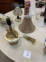 Various assorted lamps, lamp shades, and decorative items on table including a small brass and ceramic base lamp and multiple lamp shades