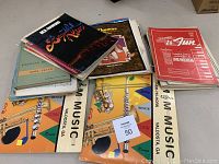 Lot of piano and flute music books and sheet music, stacked and fanned on a table, showing covers and titles
