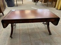 Full view of closed drop leaf table showing leather top and mahogany wood construction on carpeted floor.