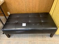 Photo of black rectangular ottoman from above showing overall condition and button-tufted top.
