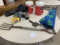 Photo showing all items in lot: two red and white Igloo coolers, Trudeau flask, Eveready flashlight, garden pitchfork, splitting maul, two blue floral folding chairs, and an additional small item