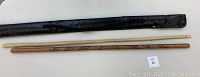 All three items: the plain stick, carved stick, and black carrying case on a white surface