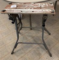 Full front view of vintage Black and Decker Workmate portable workbench showing worn wooden slat top with old paint and metal frame with legs and plastic clamping handles.