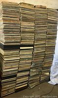 Five tall stacks of vinyl record sleeves piled on a floor against a wall