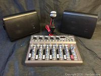 Full view of mixer with two speakers and microphone in front on black backdrop.