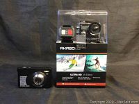 Akaso Ultra HD 4K Edition action camera in packaging next to compact digital camera showing front lens.