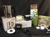 Photo showing Secura automatic milk frother with base and lid, two cat face coffee mugs (one white, one black), Kemier collapsible green water bottle in its box, and three round Aiboo lights with wire.