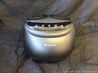 Front view showing the massager's control panel with five push buttons and two padded foot slots.