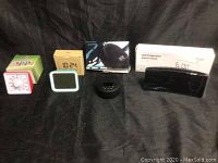 Several clocks and timers displayed against a black backdrop, including boxed LED projection alarm clock and multiple digital clocks and a black circular device.