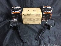 Two black LED Solar Torch Lights with ground stakes, with their respective packaging, and one boxed AmeriTop 3-head LED light in the center.