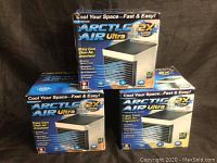 Photograph of three Arctic Air Ultra cooler boxes stacked, showing branding and product image highlights cool, clean air and 2x cooling power.