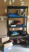 Full view of black shelving unit with household repair items including cords, tools, and boxes.