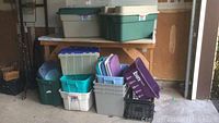 Photo showing various plastic storage bins stacked and arranged, including green, beige, gray, white, purple, and black colors with some lids and a black crate.