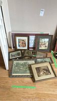 Nine vintage framed prints and framed textile arranged on the floor against a wall, showing variety of subjects and frame styles.