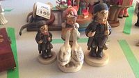 Three Hummel figurines displayed on a table, including two boys and one girl with geese.