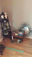 Shows tiered mahogany corner shelf with floral arrangement, camera and figurines on shelves, small upholstered stool in front, and round ornate mirror against wall.