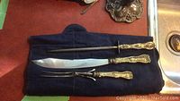 Three-piece sterling handled carving set including knife, fork, and sharpening steel displayed on navy cloth.