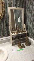 Brass bells on and around a white wood cabinet with a mirror, displayed on shelves and countertop.