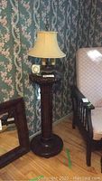 Full view of the dark carved mahogany stand with vintage lamp on top in corner of a room.