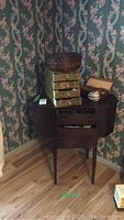 Full view of dark wooden sewing table topped with wicker basket, tin organizer and trinket box